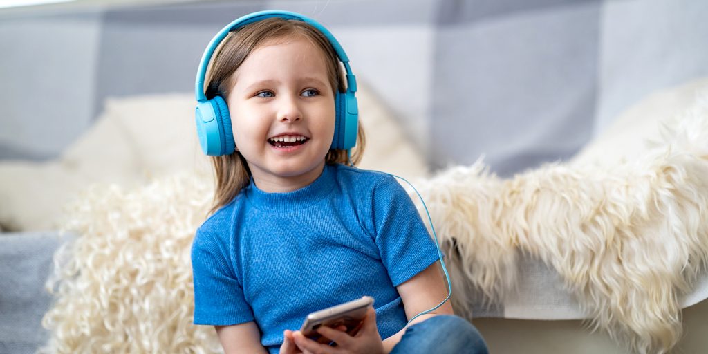 Stories for kids Alt description: A little girl laughs while listening to a podcast with headphones.
